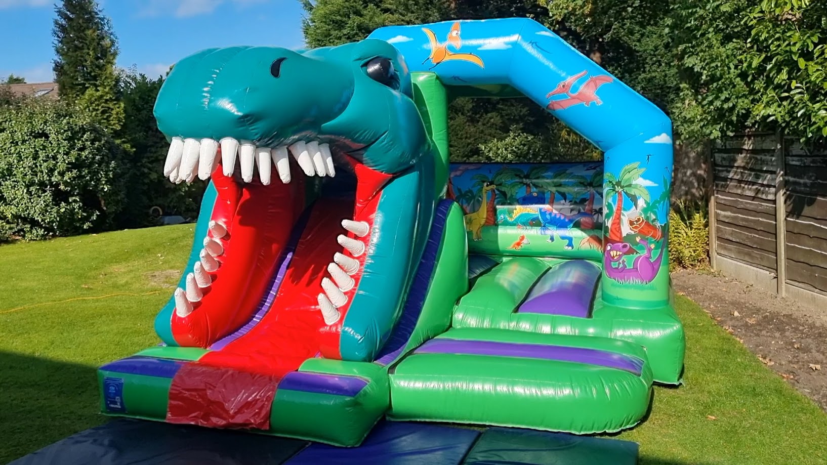 Bouncy Castle Hire Bredbury, Romiley & Marple - Born 2 Bounce Alt Text: > 3D Dinosaur Bouncy Castle with slide setup for a garden party in Romiley, SK6.